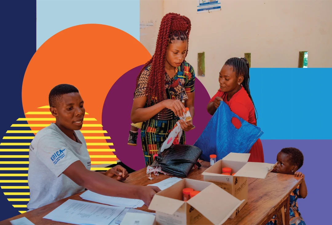 A health worker, sitting at a table, helps organise health supplies while a woman standing in a colourful dress hands out health supplies to another woman who is handling a plastic bag, while a child watches nearby