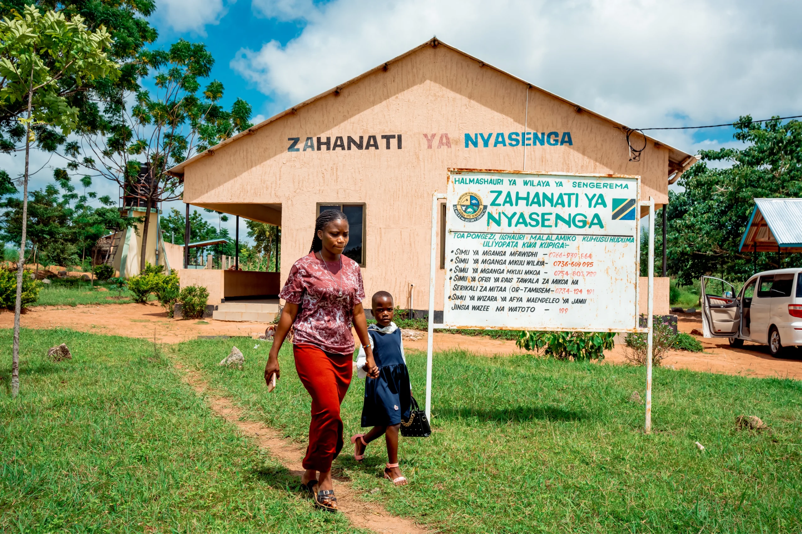 A woman and a young child holding hands walk away from a small rural healthcare facility